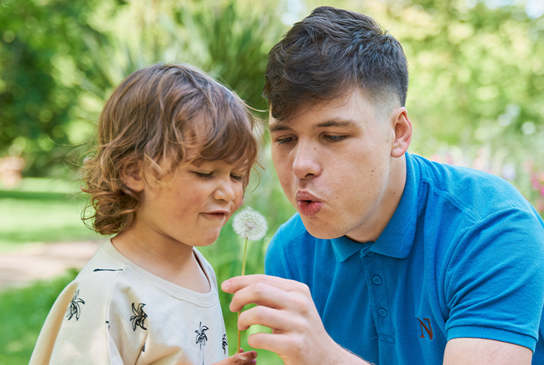 a male Norland student blowing a flower with a little boy