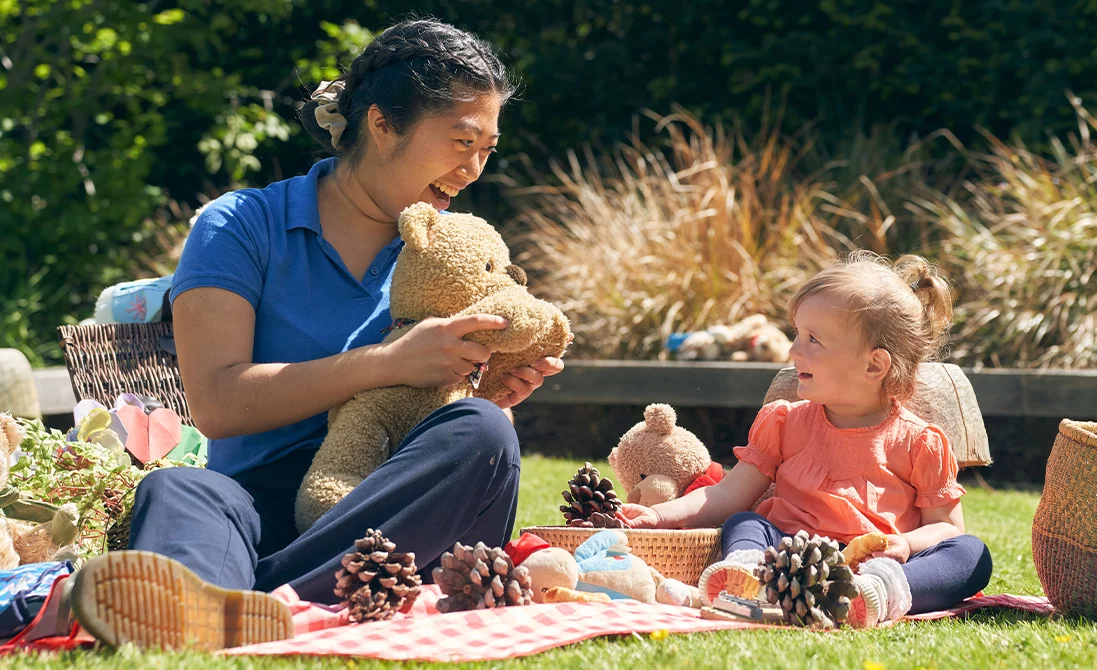 a female Norland Nanny student with a teddy bear and a child