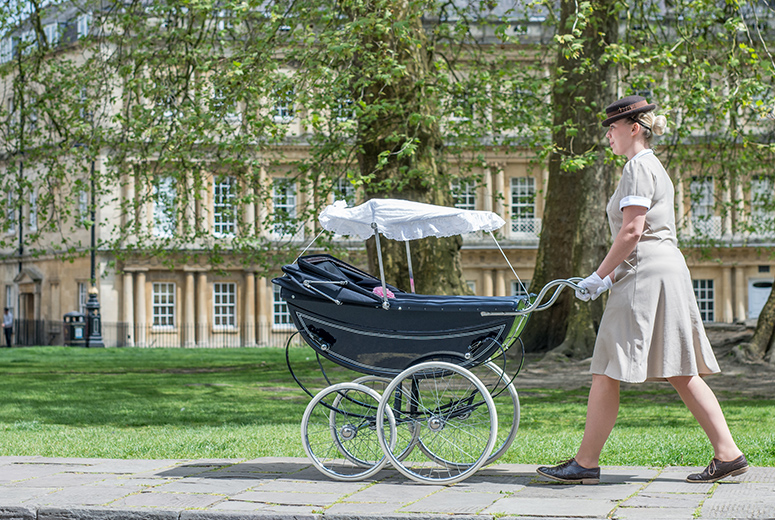 female Norland nanny in uniform pushing silver cross pram